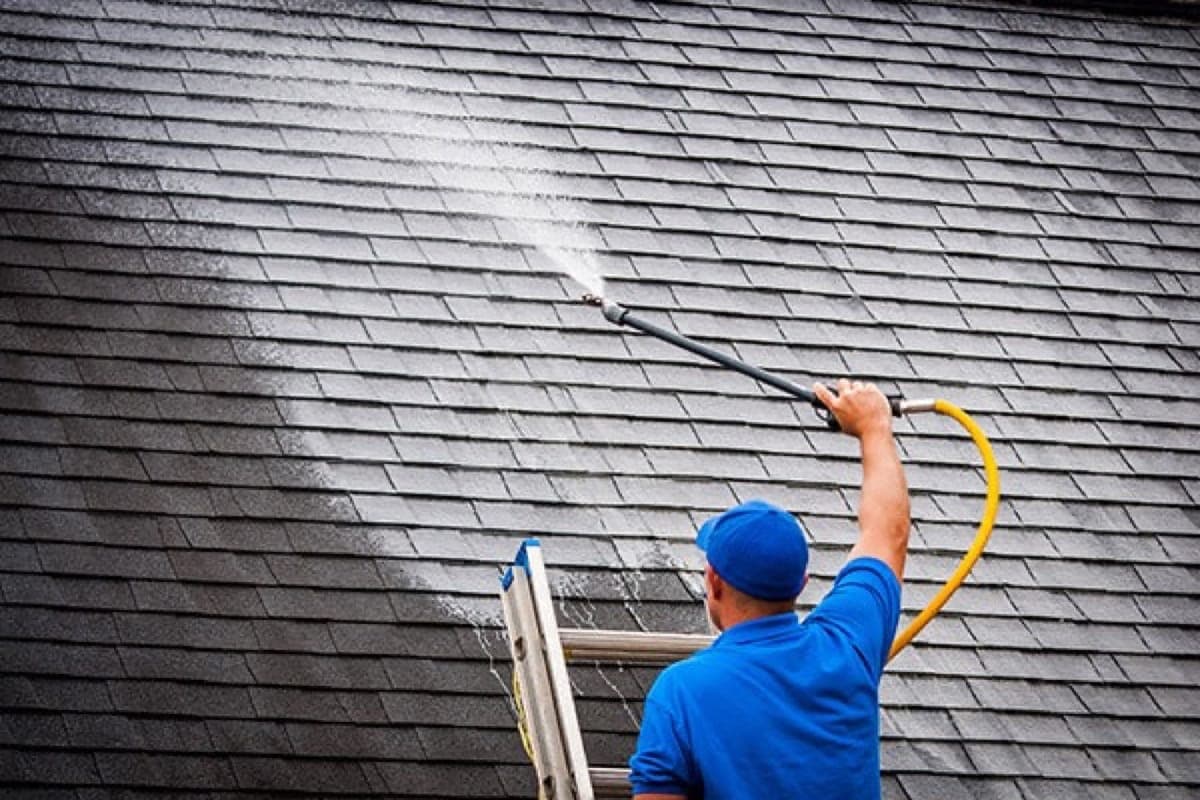 Technician spraying roof shingles during professional roof cleaning